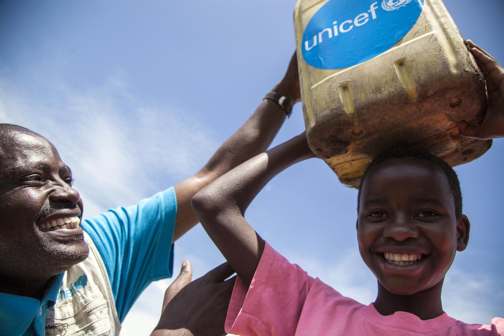 UNICEF WASH Officer helps place a bucket of clean water on a girlu2019s head Ituri DRC