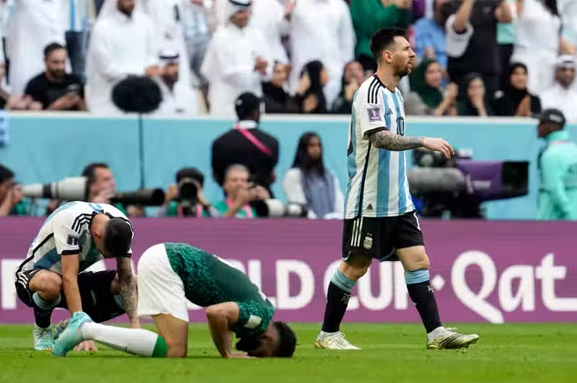 Saudi Player (in green) prostrate after winning, whereas Argentinian player sitting upset, while Messi walking out of the ground.