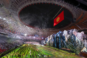 Performers fill a packed stadium field during a World Nomad Games ceremony with a large Kyrgyzstan flag hanging over a mountain stage