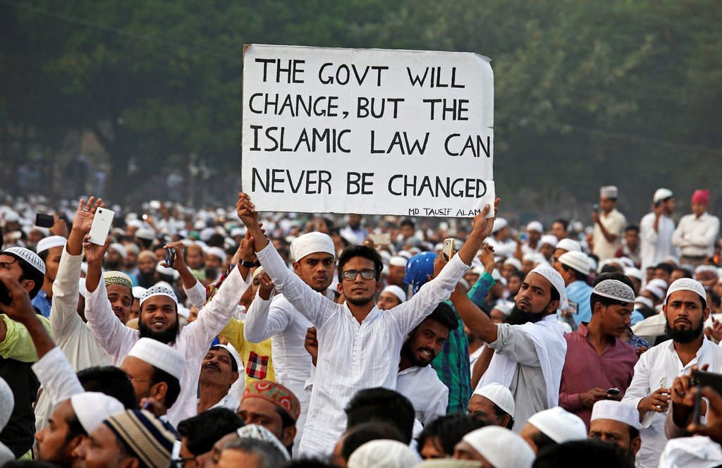 A man in a crowd holds a sign reading, The Indian govt will change, but the Islamic law can never be changed