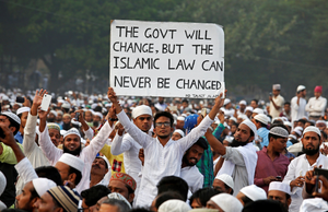 A man in a crowd holds a sign reading, The Indian govt will change, but the Islamic law can never be changed
