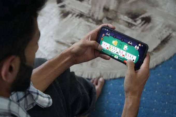 Over-the-shoulder view of a man holding a smartphone and playing an online card game