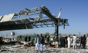 People walking through scattered debris at a train station platform under a severely damaged metal roof structure