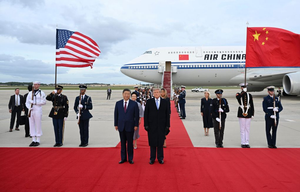 Xi Jinping and Donald Trump stand on a red carpet at an airport, flanked by honor guards holding US and Chinese flags