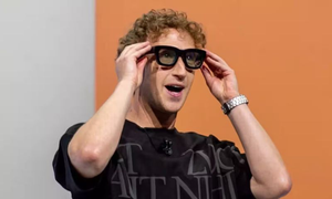Mark Zuckerberg wearing thick black smart glasses on stage during a presentation of Meta AI Tools and Smart Glasses