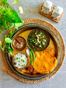 Pakistani thali featuring sarson ka saag, makki ki roti, dal makhani, rice, and green chilies served on a brass platter