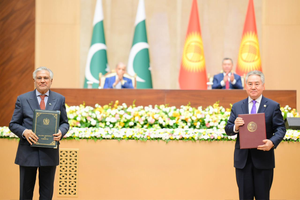 Two officials display signed agreement documents in front of the flags of Pakistan and Kyrgyzstan