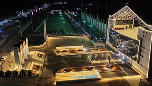Aerial photograph at night showing a brightly lit building complex and central plaza with fountains on the shores of Lake Issyk-Kul during the Echo of Nomads Festival