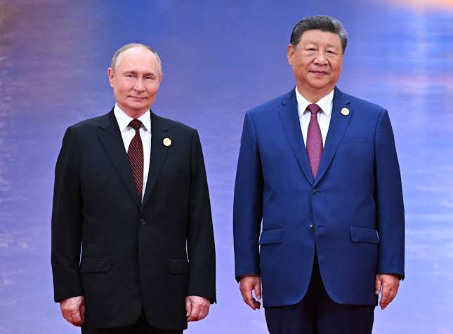 Vladimir Putin and Xi Jinping standing side by side in suits against a blue background