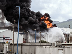Due to Iran War, Thick black smoke and flames rise from an industrial facility as high-pressure water streams are sprayed onto the fire