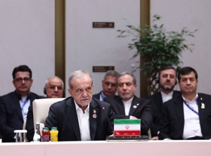 Iranian President Masoud Pezeshkian speaks at a conference behind an Iranian flag placard